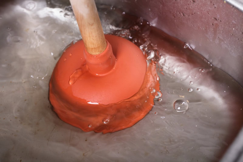 Homeowner trying to unclog a drain with a plunger in their Escondido, California home.
